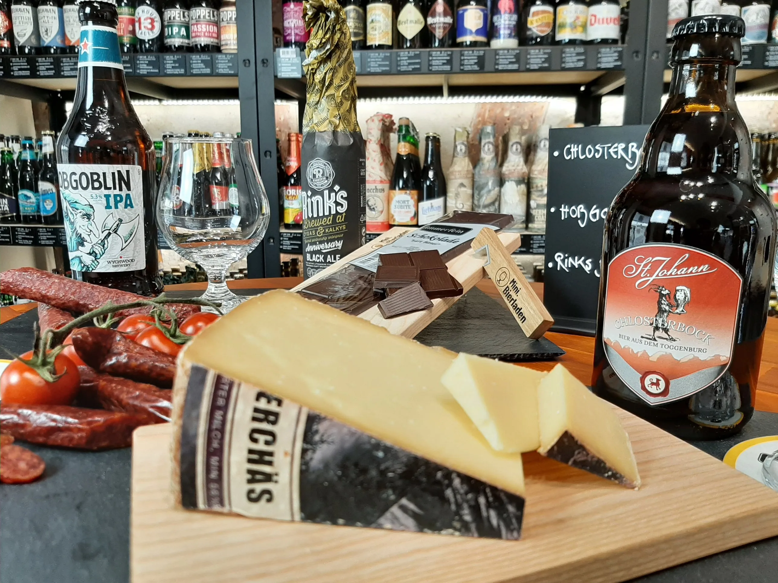 Bierflaschen, Käse, Trockenwurst und Schokolade auf einem Holzbrett im Laden